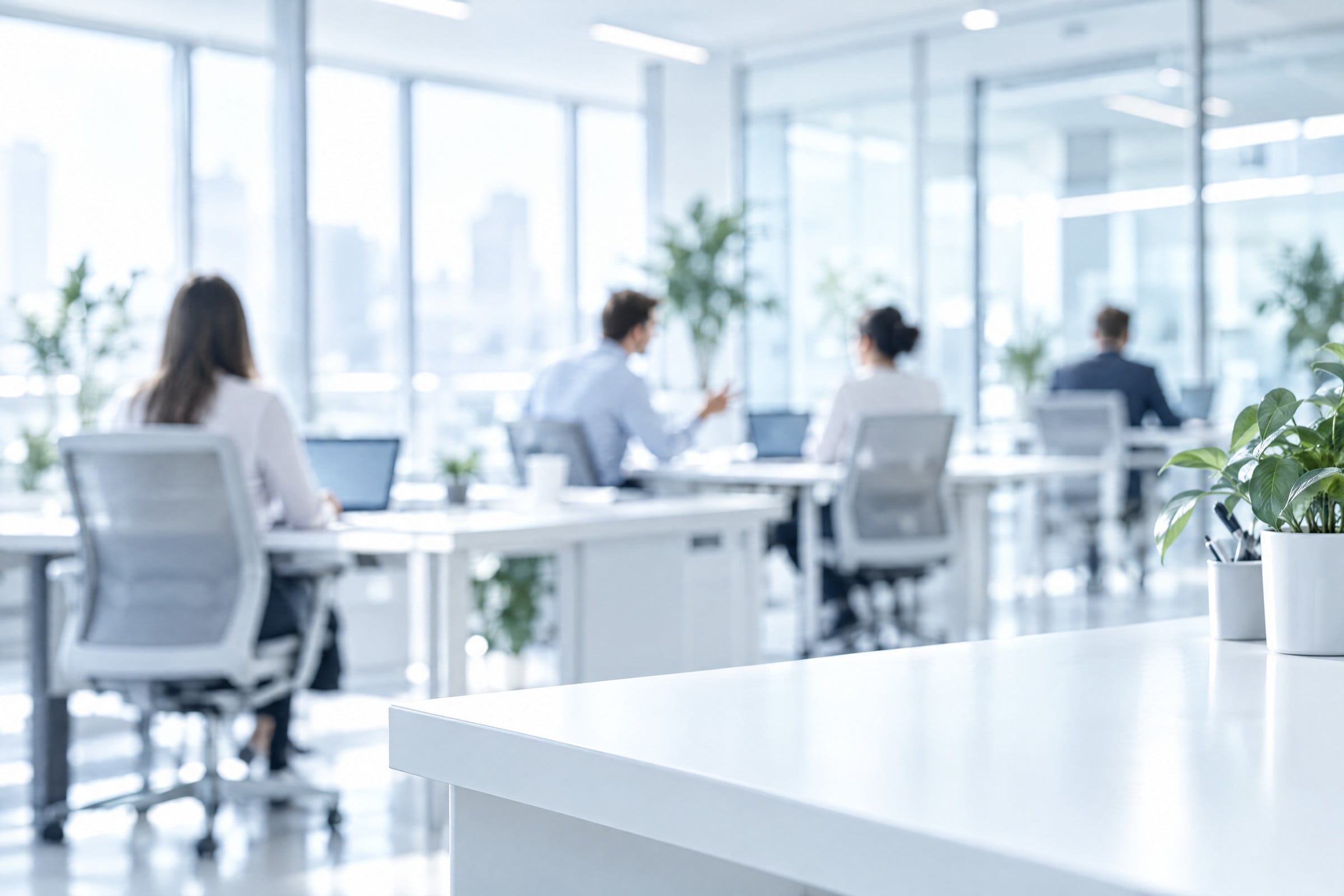 Una oficina luminosa con varias personas trabajando, de espaldas y desenfocadas.